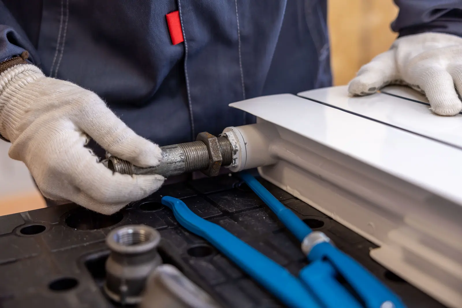 Des mains gantées serrent un raccord sur un tuyau de chauffage.