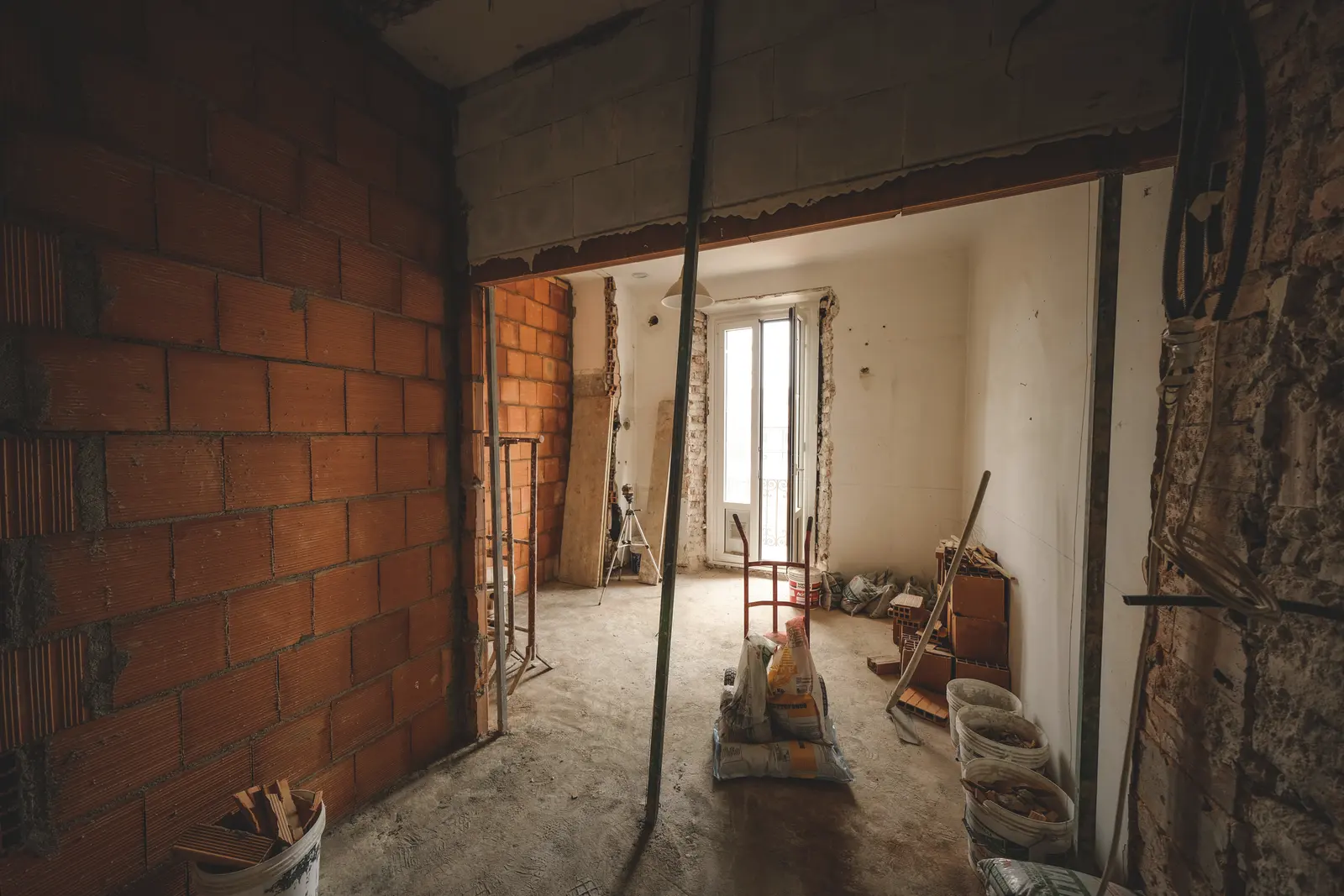 Un appartement en travaux : cloison de briques montée, étai, sacs de mortier.
