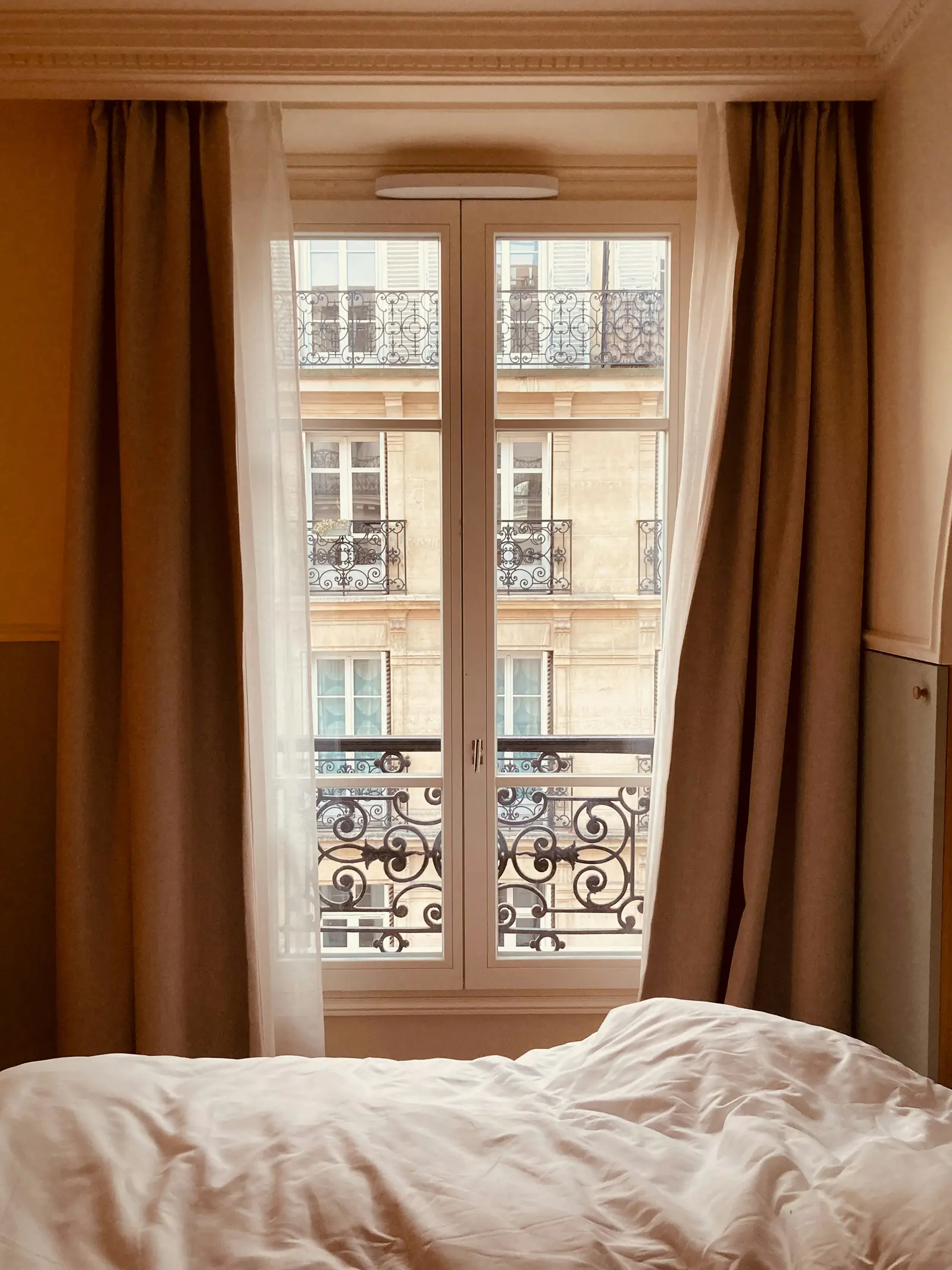 Une chambre à Paris : porte-fenêtre, rideaux tirés, les balcons en fer forgé d’en face.